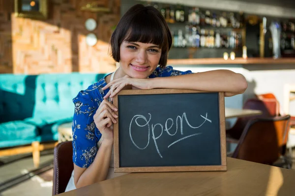 Femme souriante assise dans le café avec un panneau ouvert — Photo