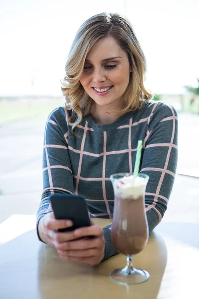 Woman using mobile phone while having milkshake — Stock Photo, Image