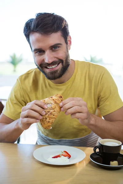 Sonriente hombre teniendo croissant en la cafetería —  Fotos de Stock