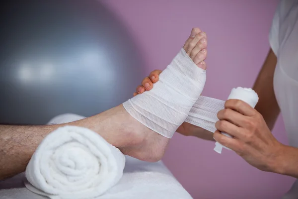 Fisioterapeuta poniendo vendaje en los pies lesionados del paciente — Foto de Stock