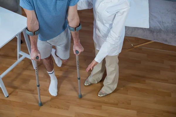 Fisioterapeuta ajudando o paciente a andar com muletas — Fotografia de Stock