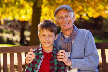 Grandfather sitting with grandson at park clipart