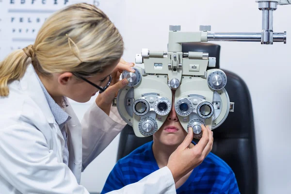 Vrouwelijke optometrist examencommissie jonge patiënt op phoropter — Stockfoto