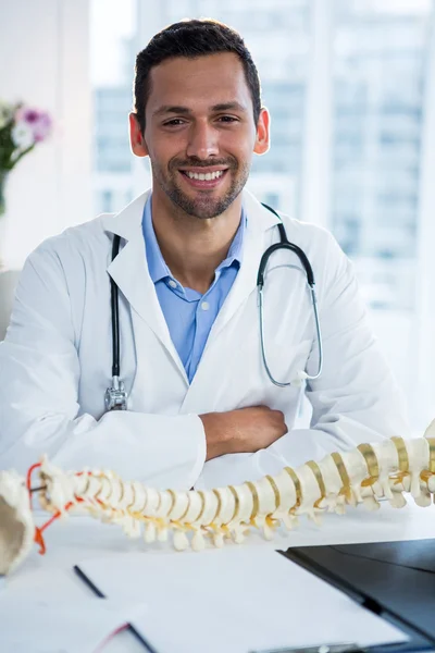 Portrait of smiling physiotherapist sitting with spine model — Stock Photo, Image