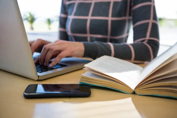 Vrouw met laptop met mobiele telefoon en roman op tafel — Stockfoto