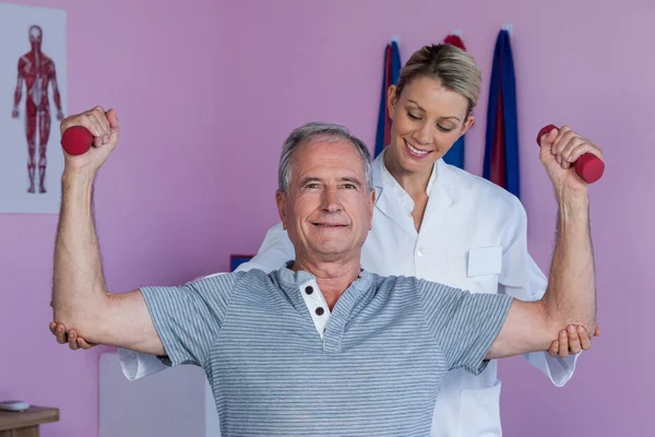 Sjukgymnast hjälpa ledande mannen att lyfta hantel — Stockfoto