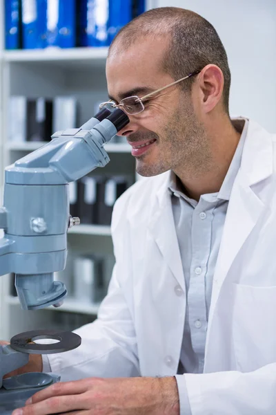 Optometrista masculino sonriente mirando a través del microscopio — Foto de Stock