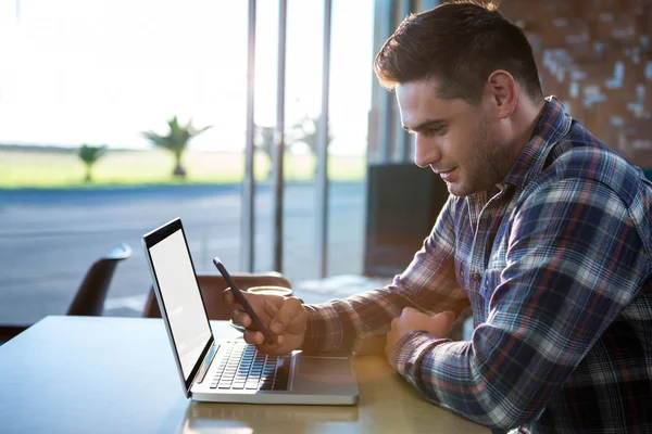 Man met mobiele telefoon met laptop op tafel — Stockfoto