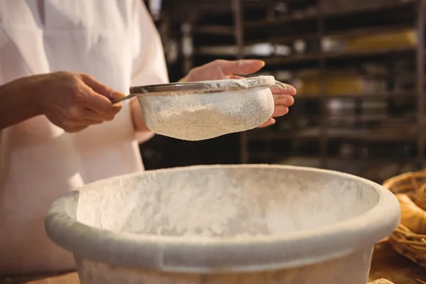 Female baker sifting flour through a sieve — Stock Photo, Image