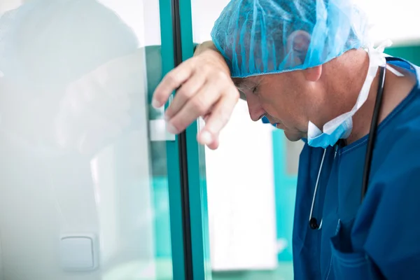 Trauriger Chirurg lehnt an Glastür — Stockfoto