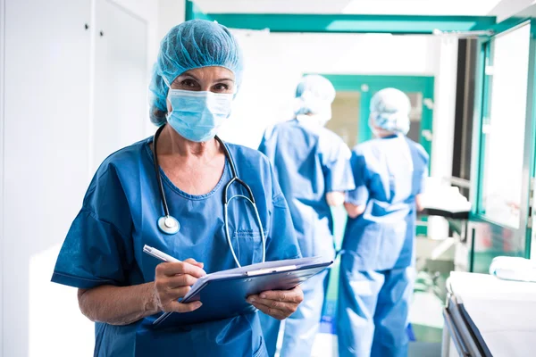 Kvinnliga kirurgen skriva på Urklipp i korridoren — Stockfoto