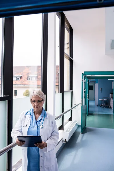 Arzt im Flur schaut auf Klemmbrett — Stockfoto