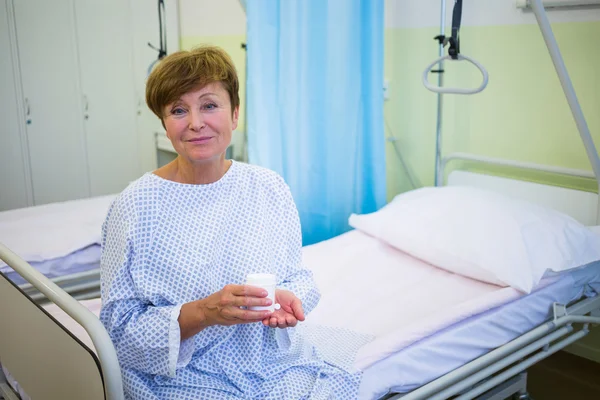 Paciente mayor sentado en una cama sosteniendo medicamentos — Foto de Stock