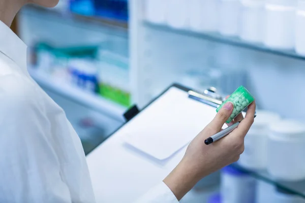 Pharmacist writing on clipboard while checking medicine — Stock Photo, Image