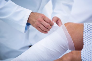 Doctor bandaging leg of patient clipart