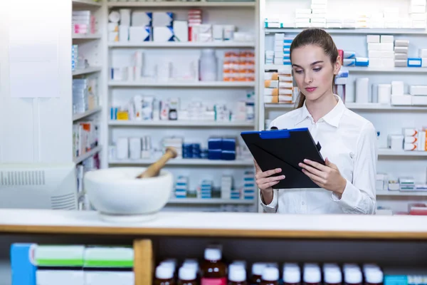 Pharmacist looking in clipboard at counter — Stock Photo, Image