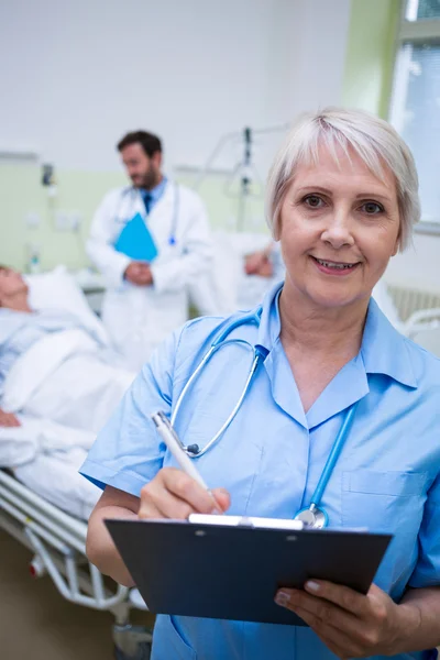 Lächelnde Krankenschwester schreibt auf Klemmbrett — Stockfoto