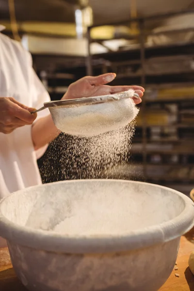 Female baker sifting flour through a sieve — Stock Photo, Image