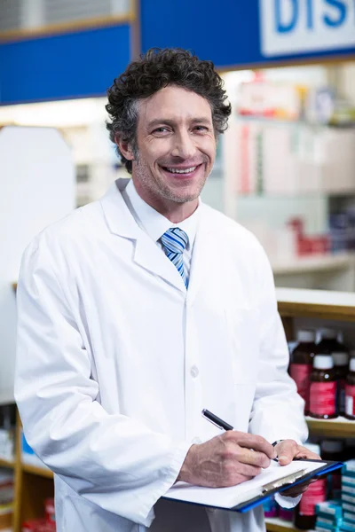 Pharmacist writing on clipboard in pharmacy — Stock Photo, Image