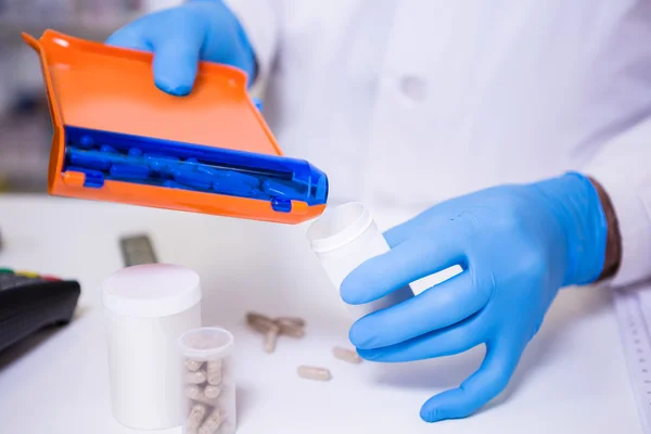 Farmacêutico colocando pílulas em recipiente — Fotografia de Stock