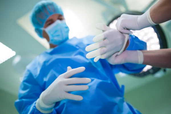 Enfermeira ajudando cirurgião no uso de luvas cirúrgicas — Fotografia de Stock