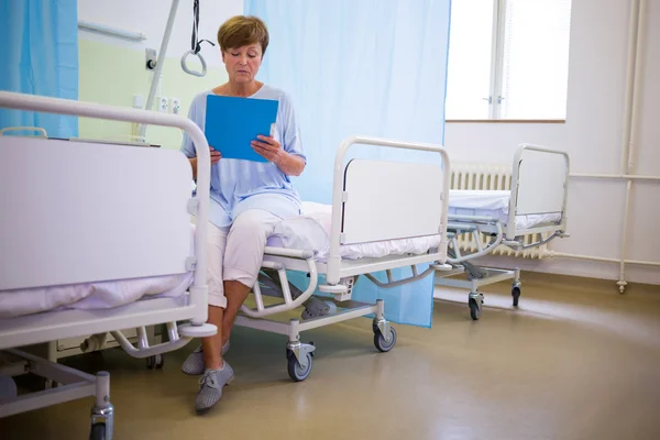 Senior patient sitting on a bed with report — Stock Photo, Image