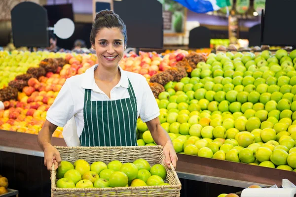 Usmívající se žena zaměstnanci, kteří zastávají košík zelené jablko v supermarketu — Stock fotografie