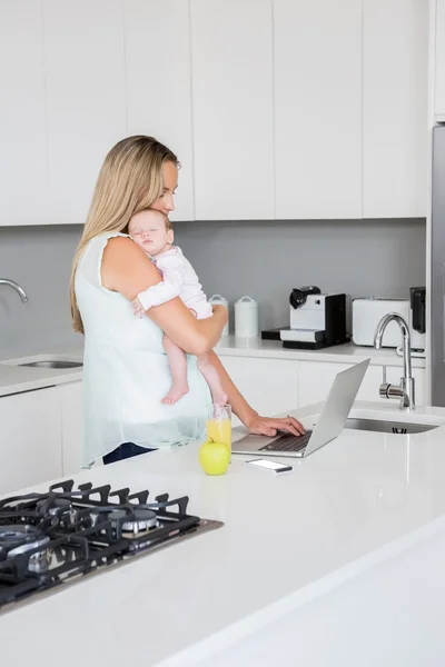 Mother using laptop while carrying baby — Stock Photo, Image