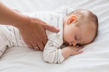 Mom putting baby to sleep in baby bed clipart