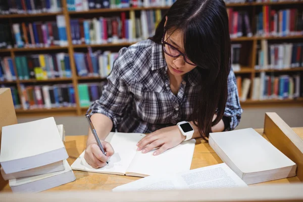 Kvinnlig student skriva anteckningar i biblioteket — Stockfoto