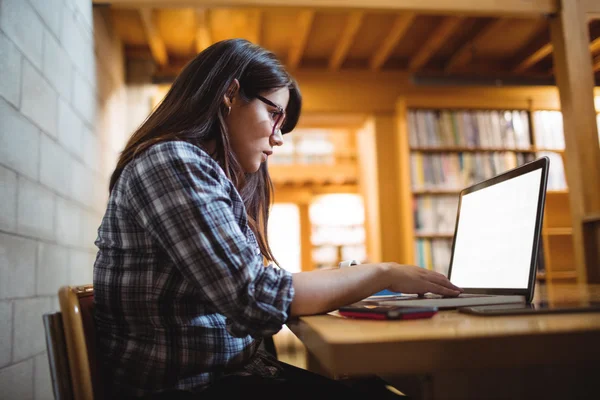 Vrouwelijke student via laptop in bibliotheek — Stockfoto