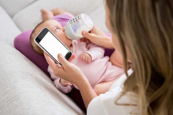Anya baba etetés közben a telefon használata — Stock Fotó