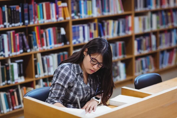 Vrouwelijke student schrijven nota's in bibliotheek — Stockfoto