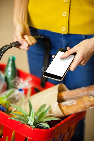 Mulher segurando mantimentos e telefone no supermercado — Fotografia de Stock