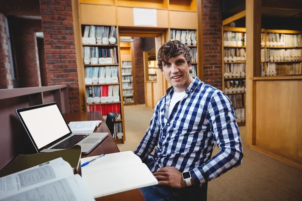 Улыбающийся студент сидит в библиотеке — стоковое фото