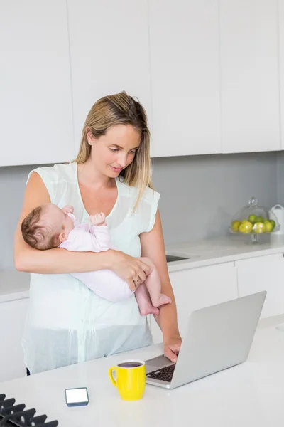 母亲抱着婴儿时使用笔记本电脑 — 图库照片