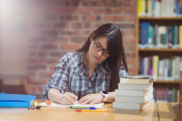 Estudante do sexo feminino escrevendo notas na biblioteca — Fotografia de Stock