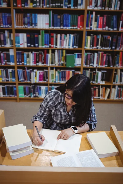 Vrouwelijke student schrijven nota's in bibliotheek — Stockfoto