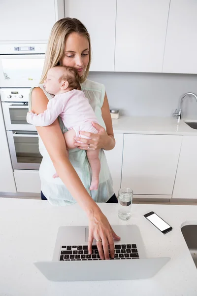 Mother using laptop while carrying baby — Stock Photo, Image
