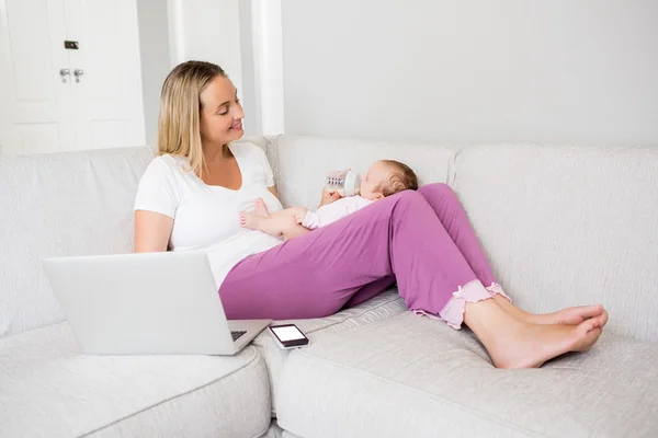 Mother using laptop while feeding baby — Stock Photo, Image