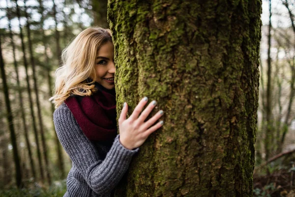 Mujer escondida detrás de tronco de árbol en bosque — Foto de Stock