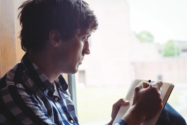 Student writing notes near window — Stock Photo, Image