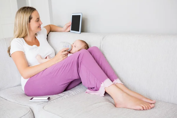Mother using tablet while feeding baby — Stock Photo, Image