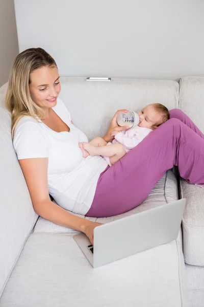 Moeder met behulp van de laptop tijdens het voeden van baby — Stockfoto