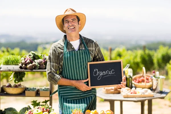 Agricultor sorridente segurando um sinal biológico — Fotografia de Stock