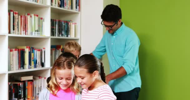 Leerkracht en kinderen lezen boeken in bibliotheek — Stockvideo