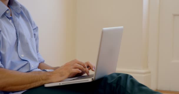 Мужчина сидит на полу и использует ноутбук — стоковое видео