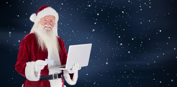Papai Noel paga com cartão de crédito em um laptop — Fotografia de Stock