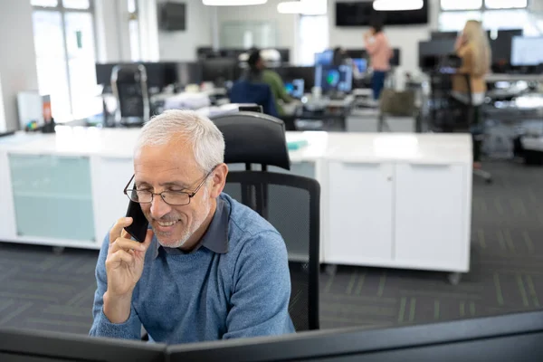 高级白种人商人戴着眼镜在现代办公室工作 坐在办公桌前 用智能手机交谈 面带微笑 Coronavirus Covid 19大流行病期间工作场所的社会疏离 — 图库照片