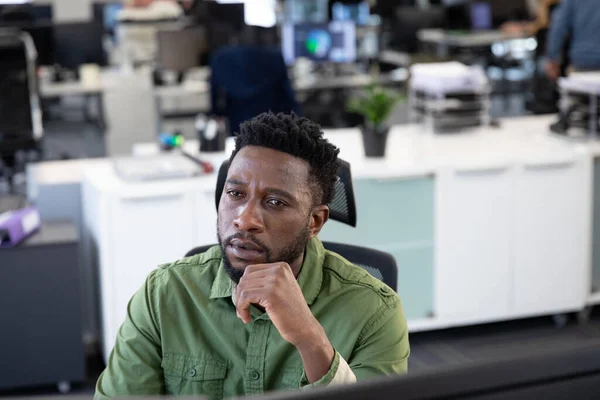 Afroamerykanin Pracujący Nowoczesnym Biurze Siedzący Przy Biurku Patrzący Ekran Komputera — Zdjęcie stockowe